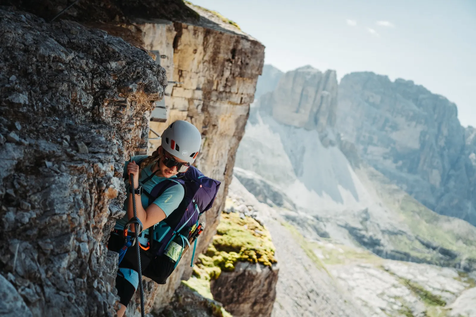 Climber in a helmet ascends a rock edge with a view of the Dolomites