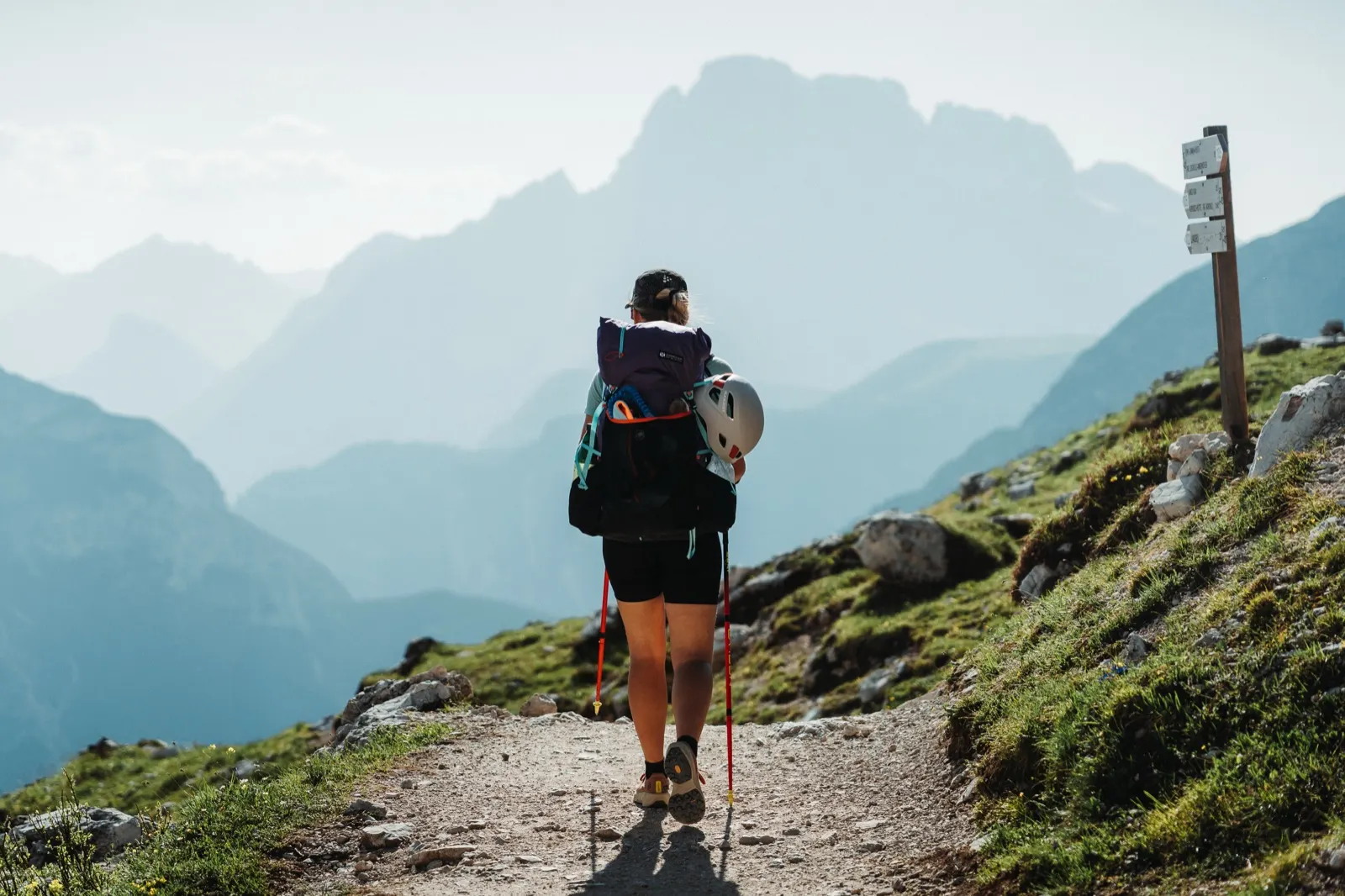 Hiker walking along a mountain path towards a signpost with the Dolomite skyline in view