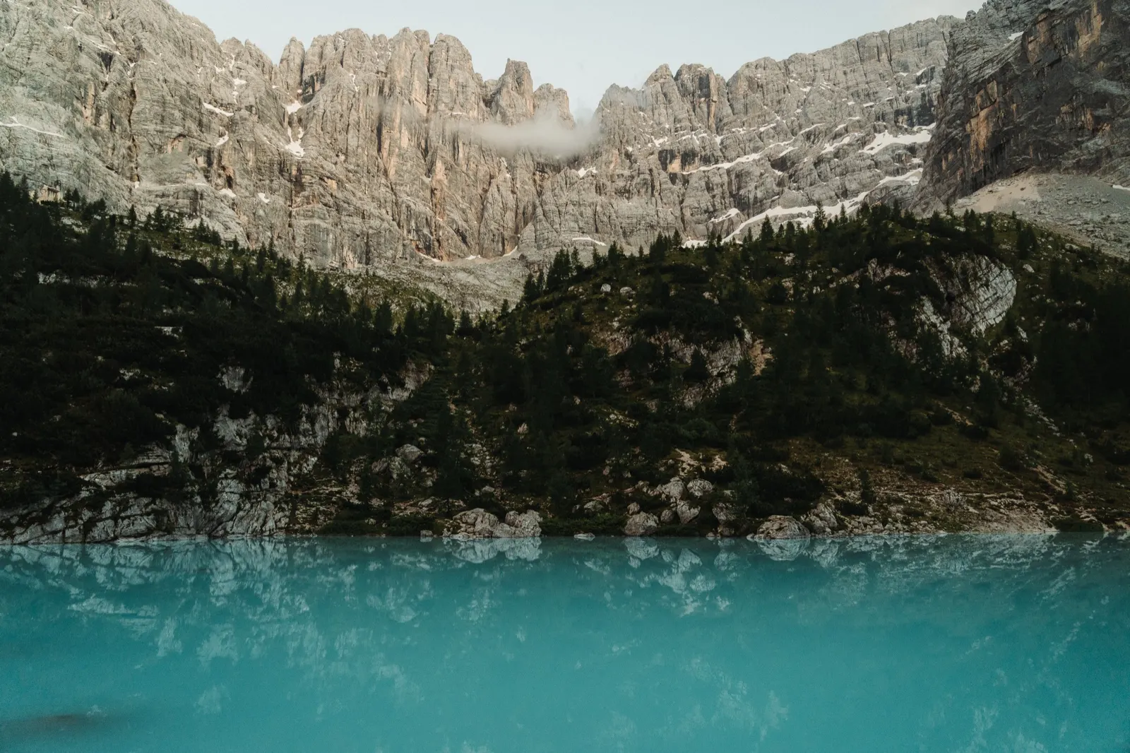 Turquoise Lago di Sorapis reflecting mountains and forest, surrounded by dramatic Dolomite walls