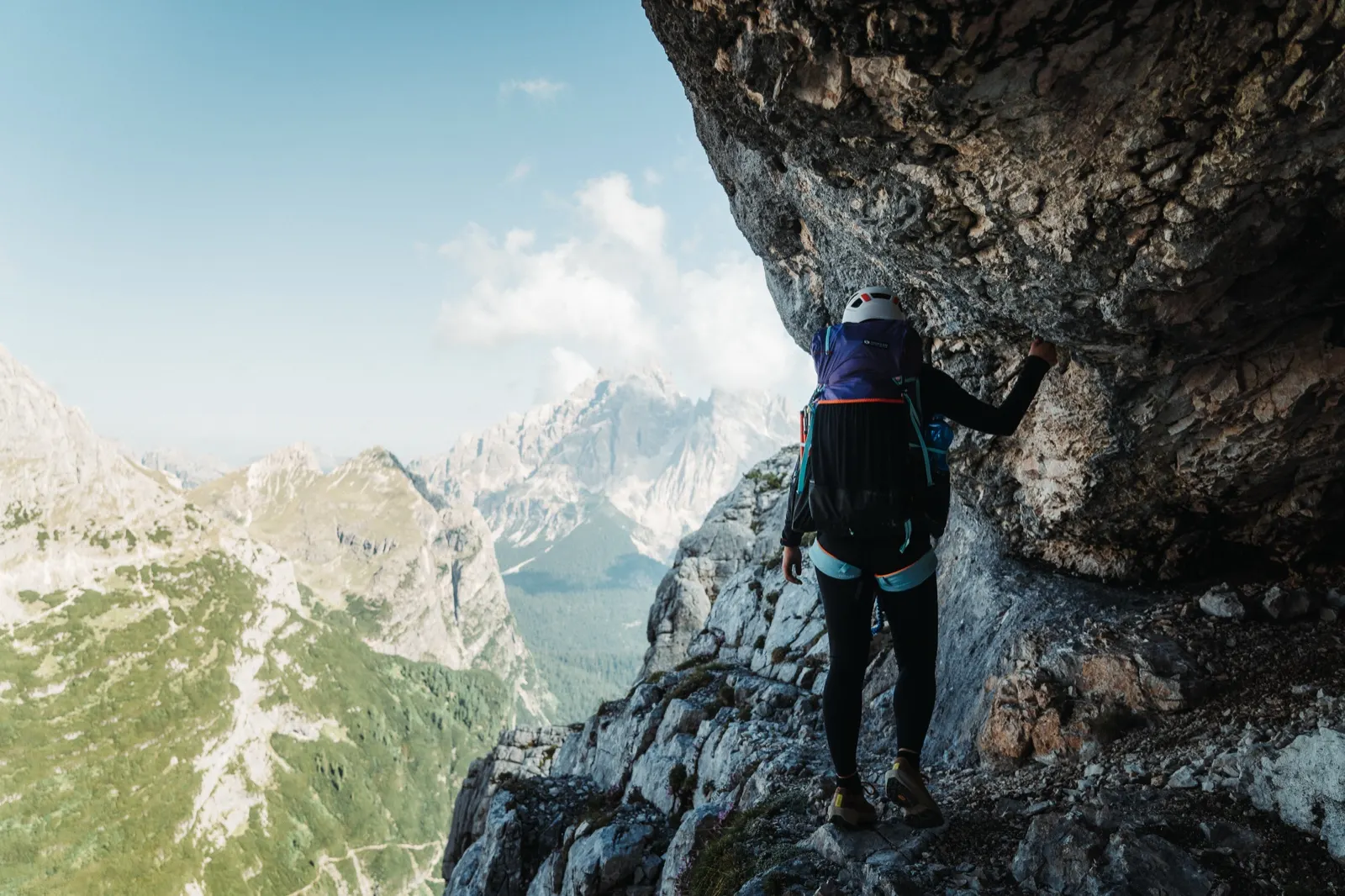 Person in a helmet and backpack walking along a rock wall