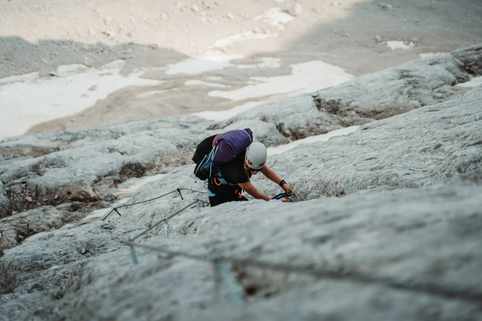 Hiker secured to a cable while climbing through a boulder field.
