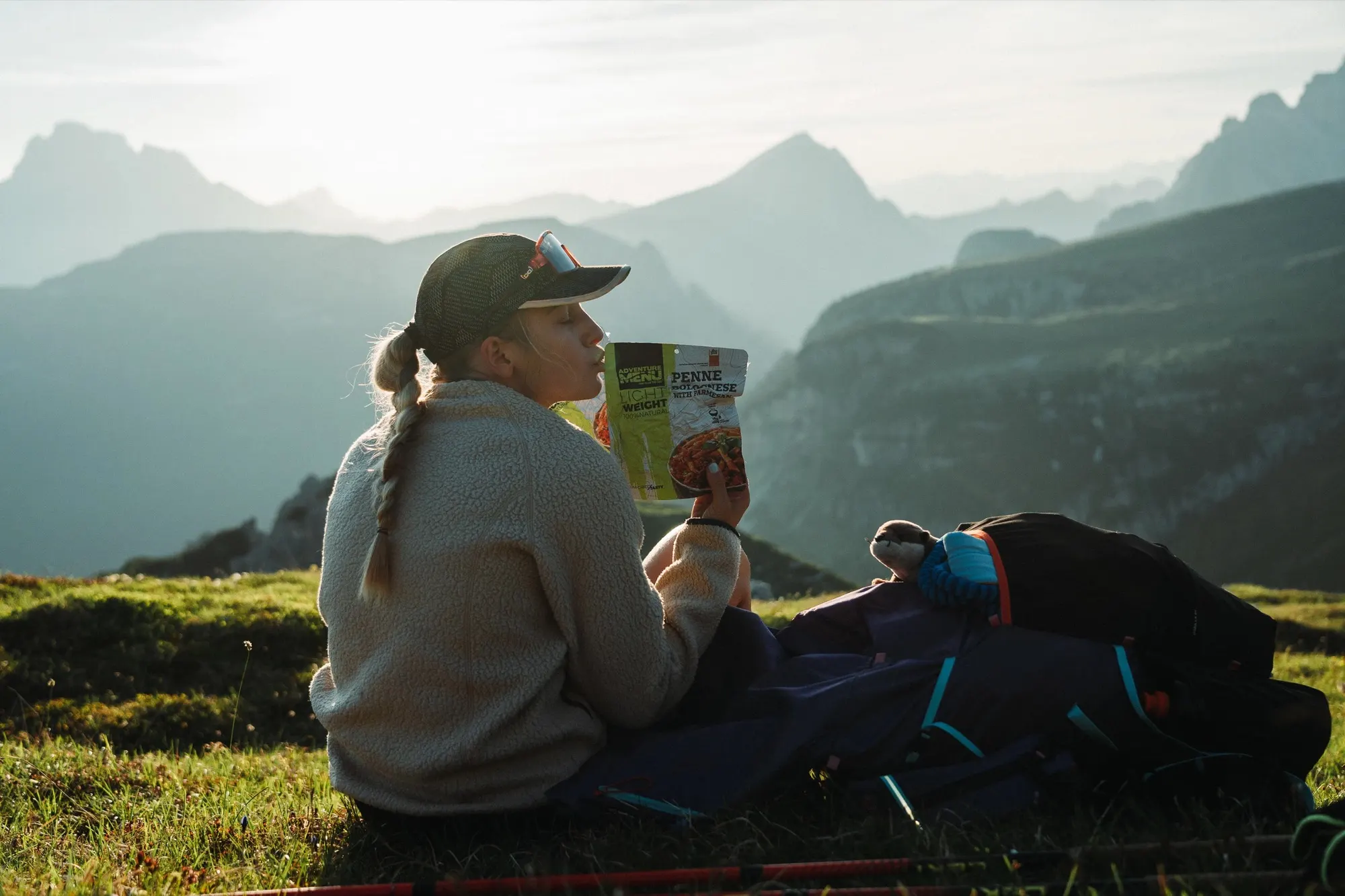 Turista sedí na horské louce při trailovém jídle, v pozadí vrcholy Dolomit