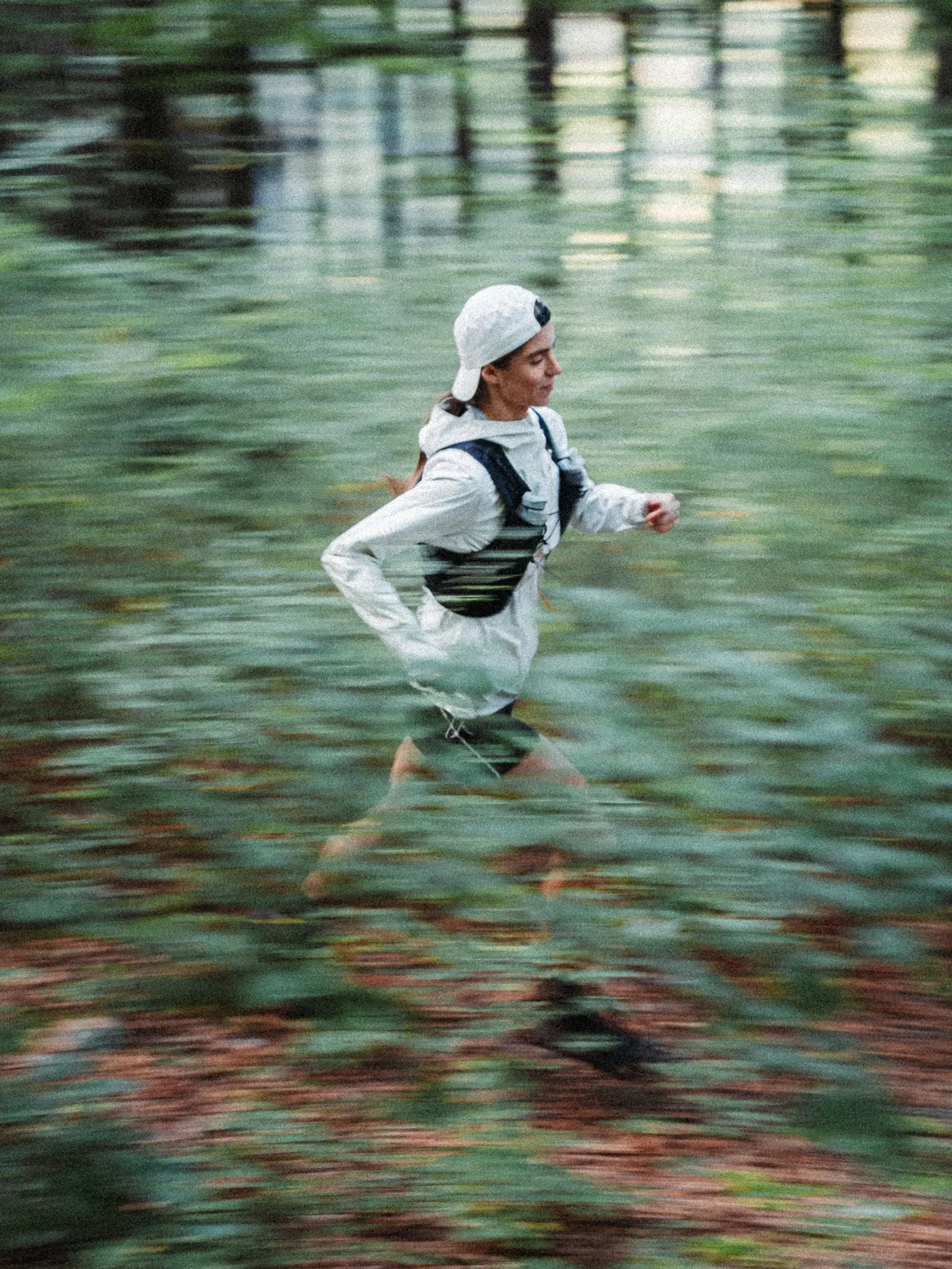 Runner in a white cap and light jacket sprinting through the forest, shot with motion blur