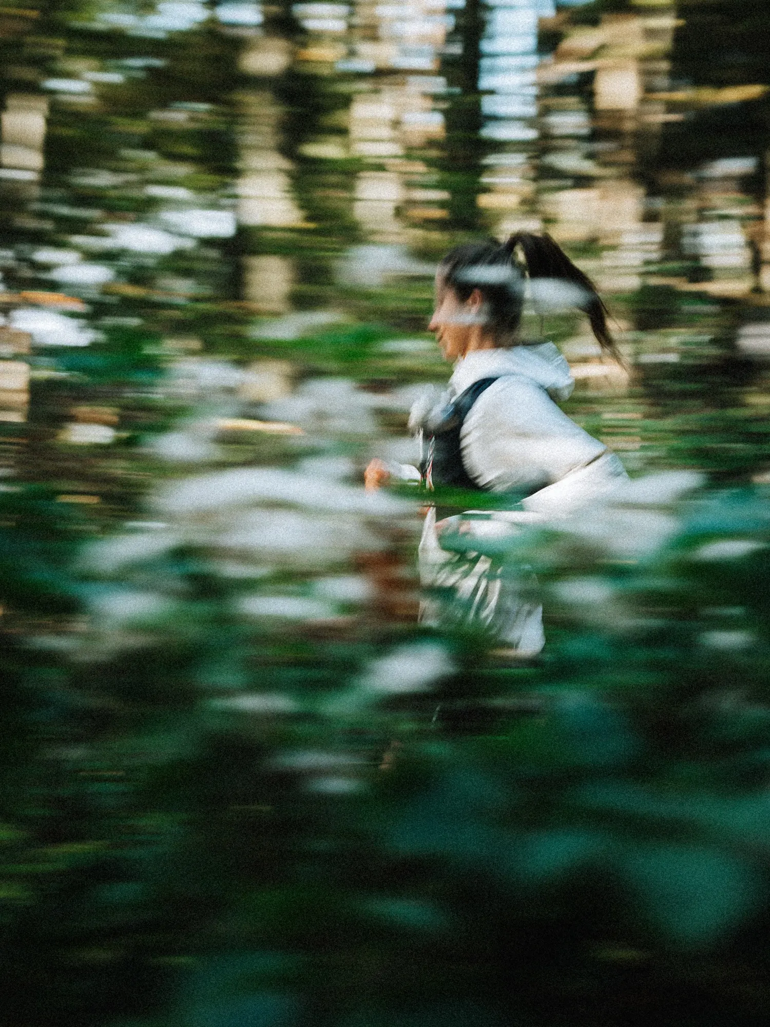 Runner in a light jacket and vest blurred against white flowers and dark foliage