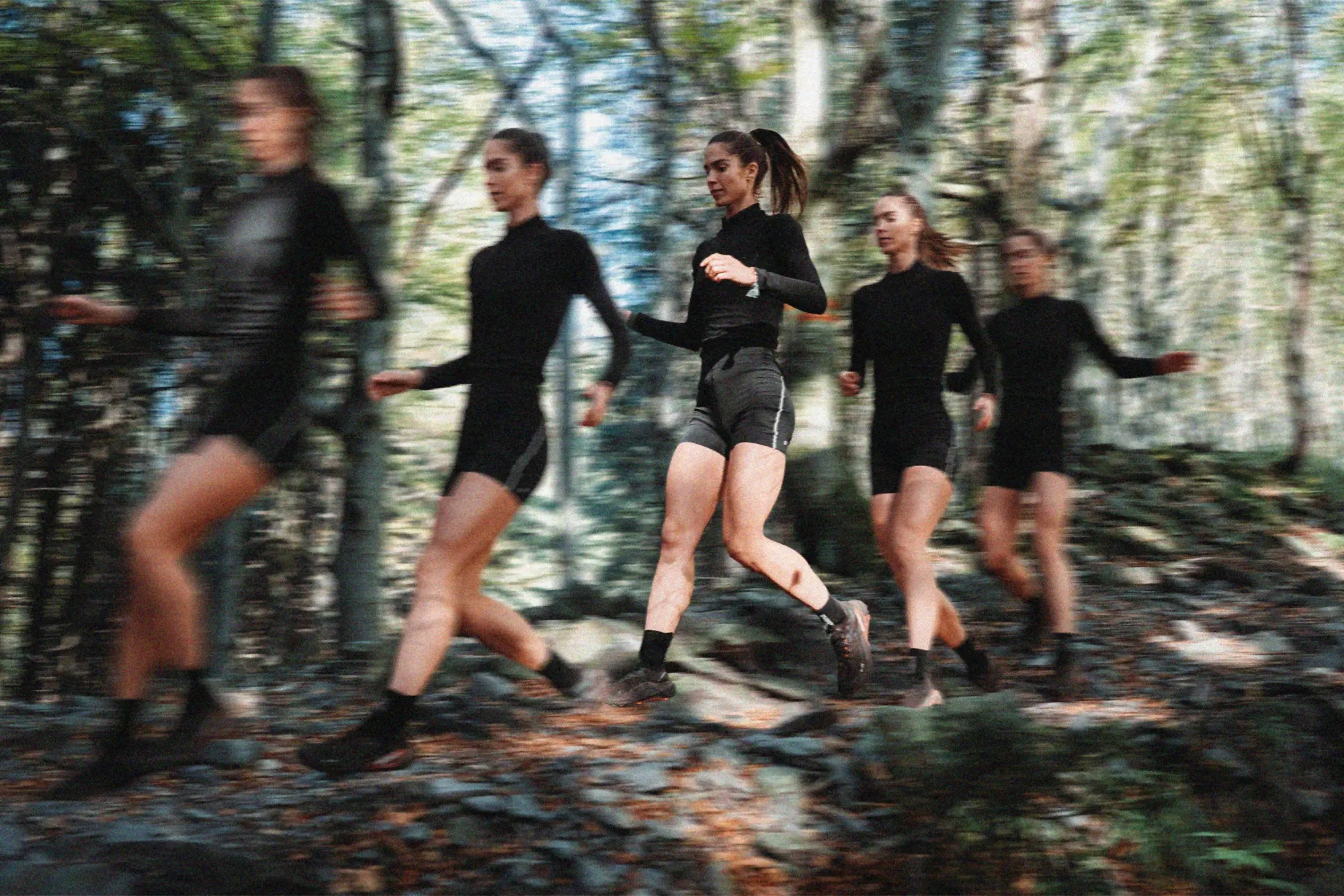Five overlapping exposures of a runner in a black top and shorts moving across a forest trail, a multiple-exposure motion composite