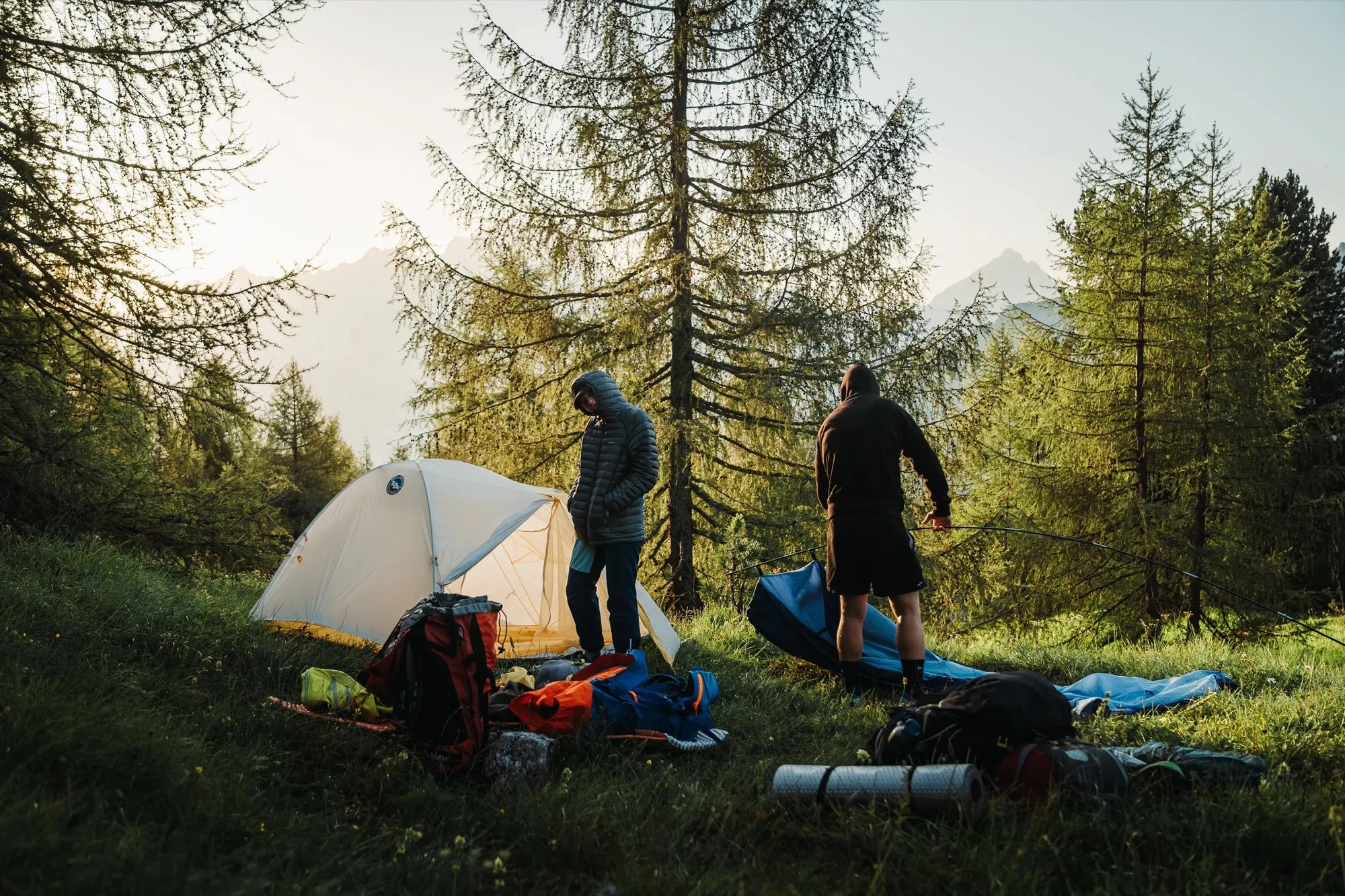Tiger Wall UL2 and camp gear in a forest clearing with two people standing nearby