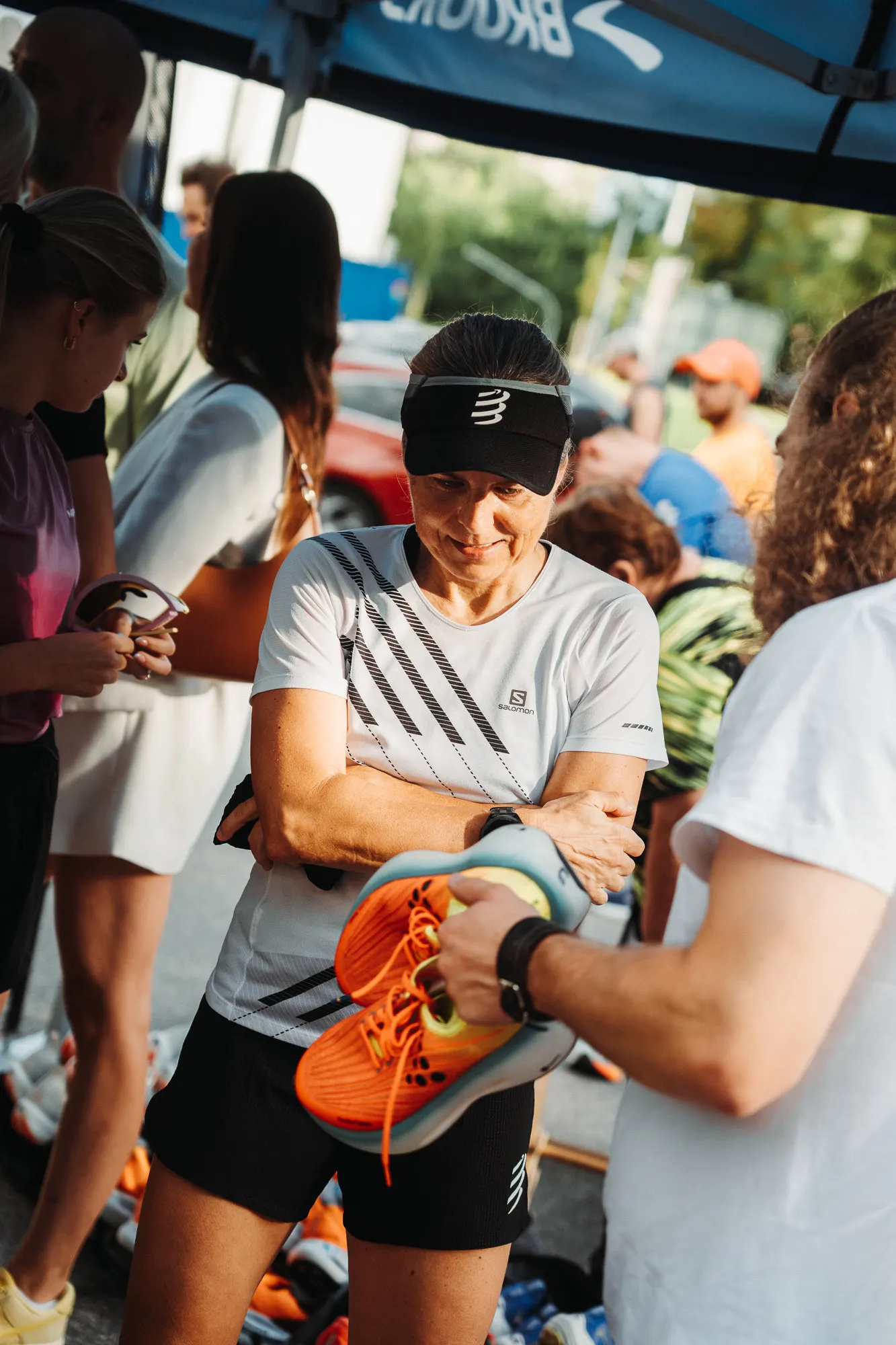 Smiling runner in a white tee holding a pair of orange running shoes