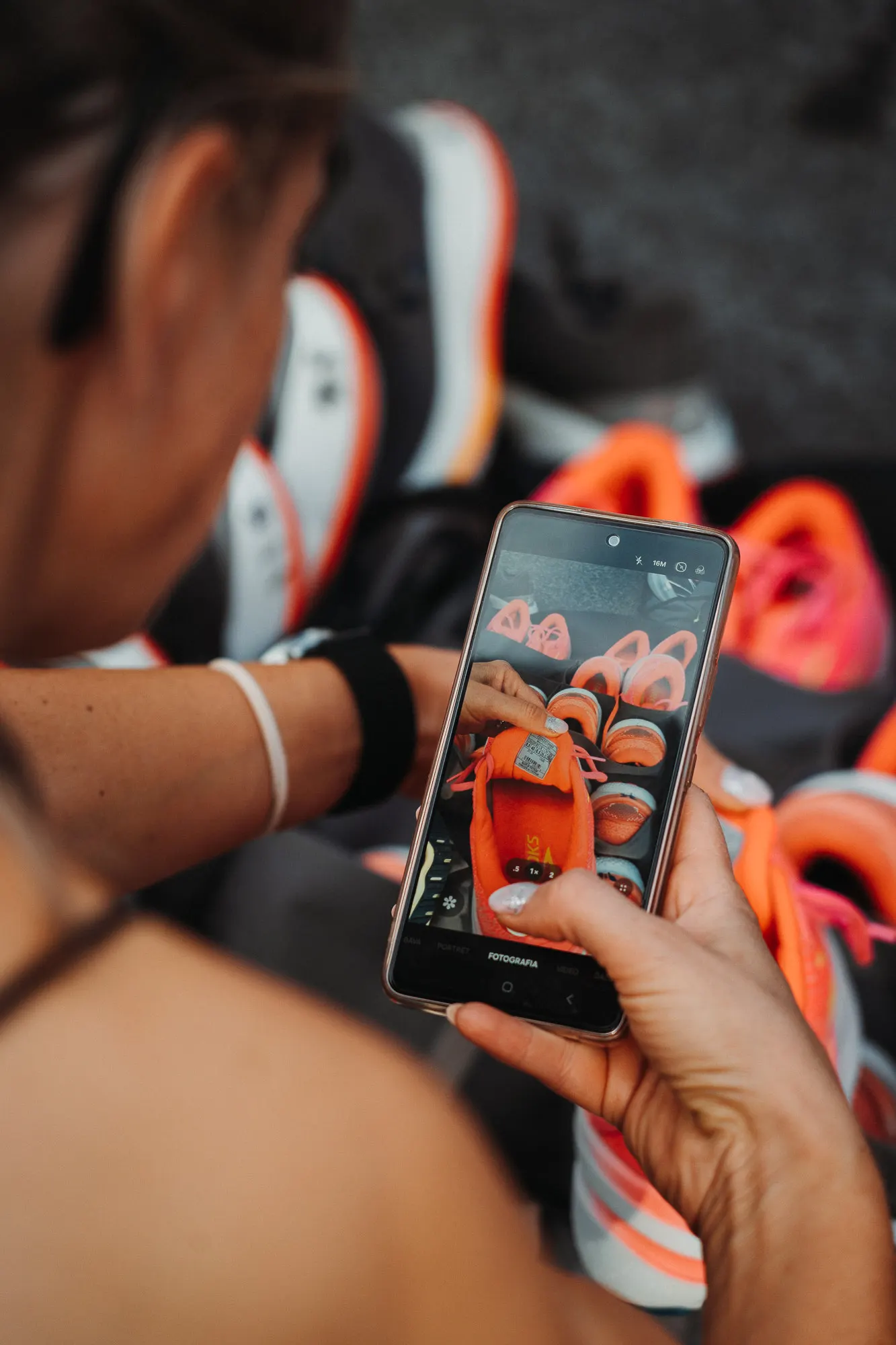 Hands holding a phone showing a photo of orange running shoes