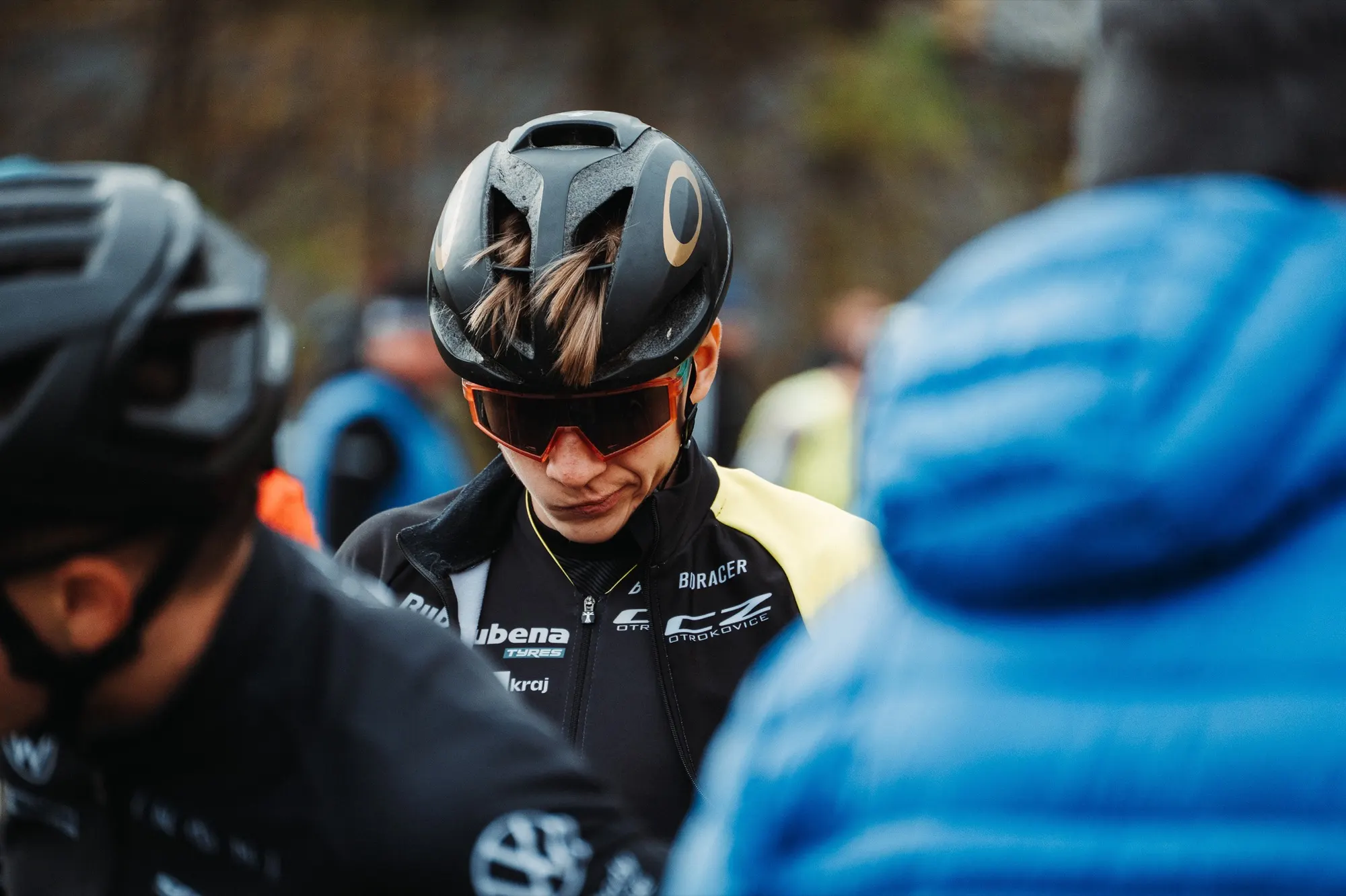 Close-up of a rider in a helmet with spectators in blue jackets behind