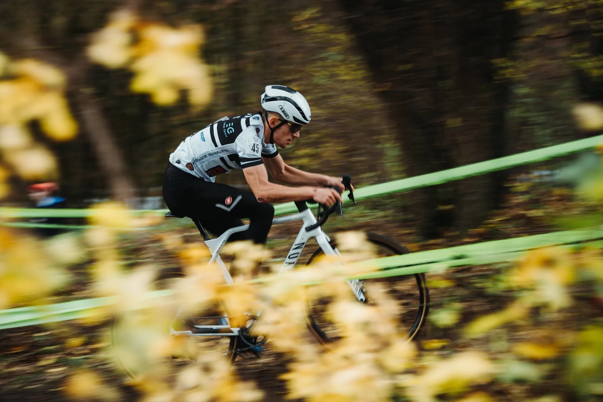 Cyklokrosař projíždí podzimním listím mezi páskami trati na Grand Prix Podbrezová