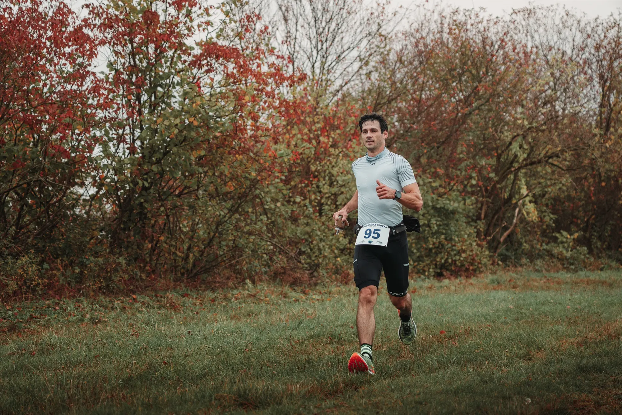 Runner running over grass beside red autumn bushes