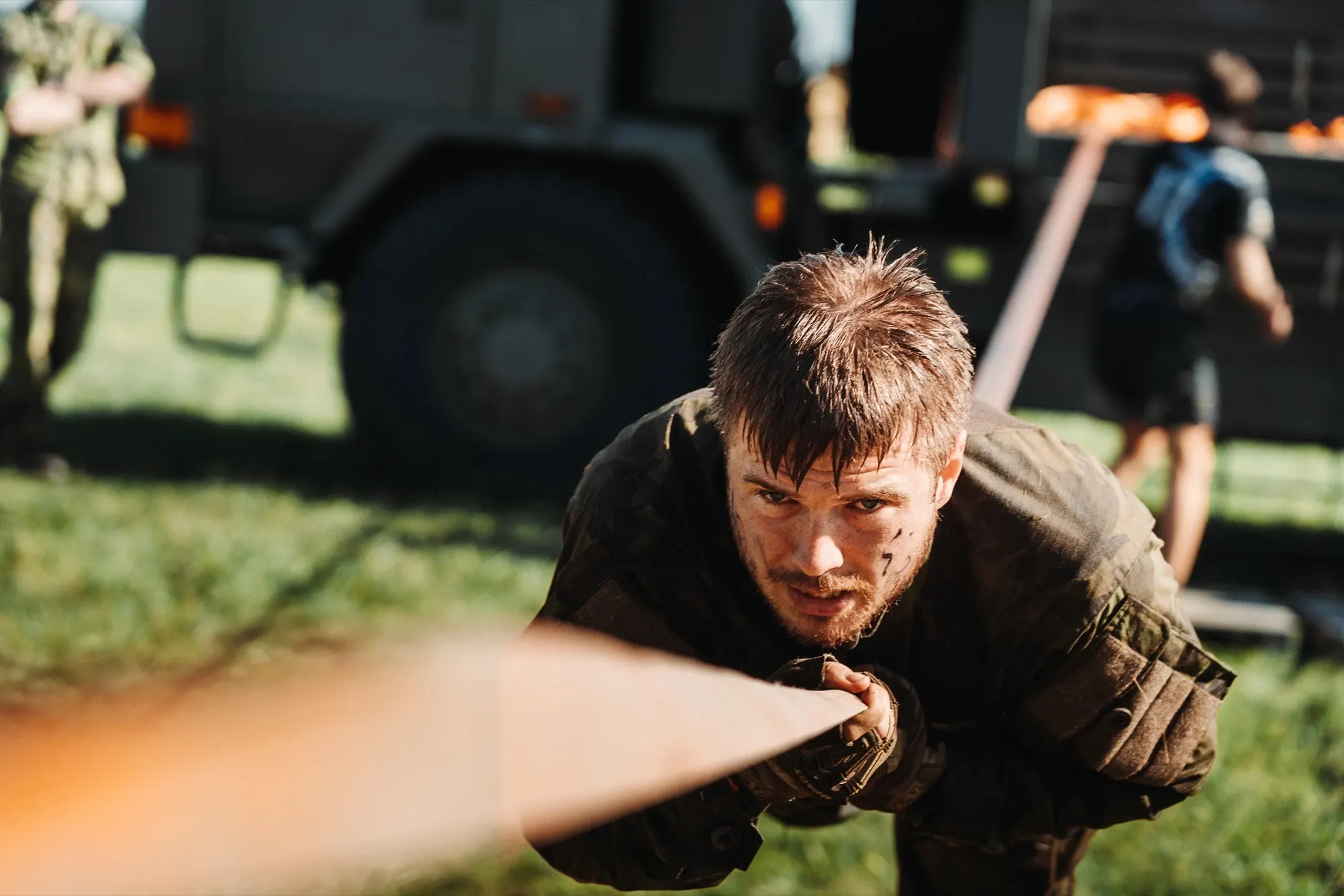 Competitor with a determined face crawling under an obstacle next to a truck
